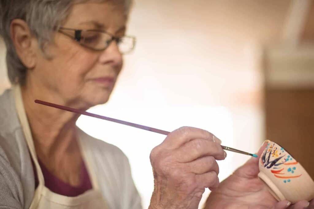 An older woman paints a ceramic teacup