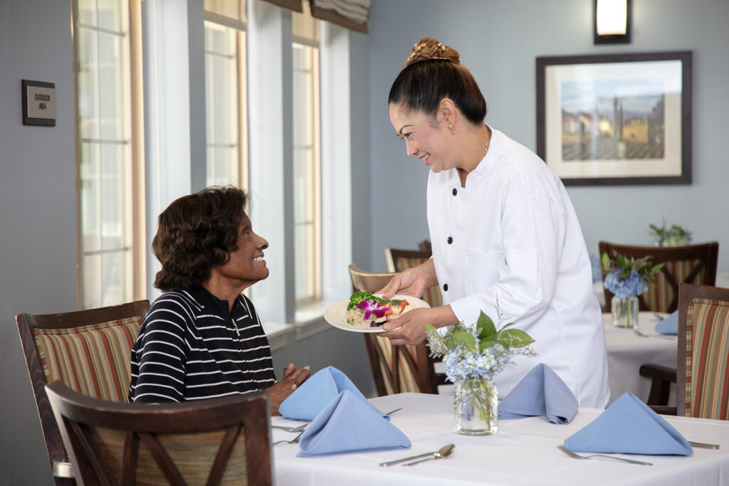 A dining server places a colorful meal in front of a resident in the dining room.