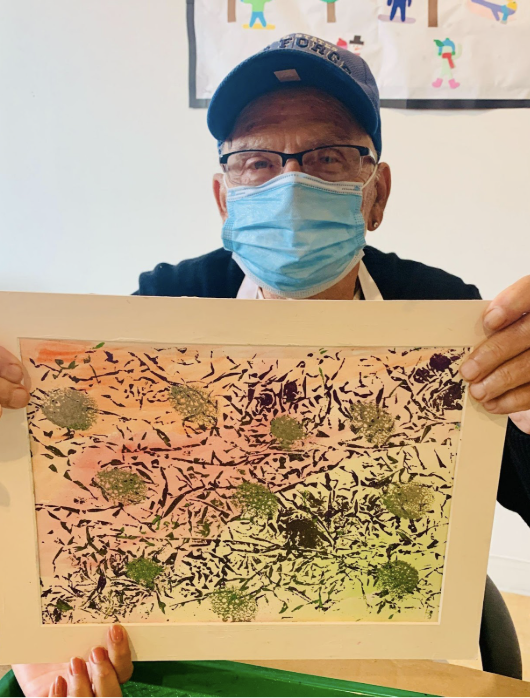 A man holds up his artistic creation, a painting with mixed textures.