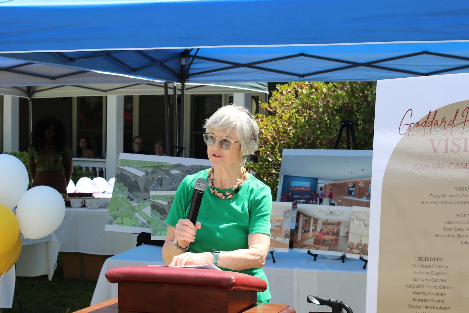 Woman with glasses speaks into a microphone at a podium outside